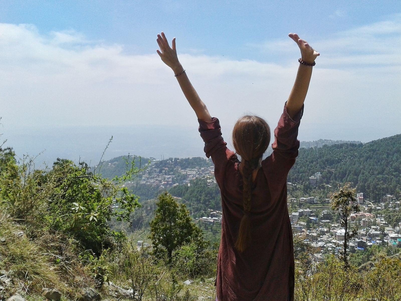 mujer joven de pie en una colina con las manos extendidas hacia el cielo azul mientras domina una ciudad